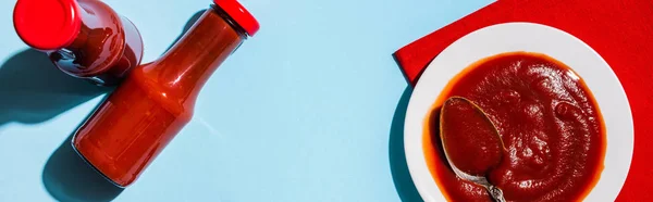 Top view of tasty ketchup in bottles and plate on blue background, panoramic shot — Stock Photo