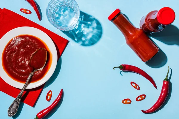 Vue du dessus de la sauce chili maison avec verre sur l'eau et piments sur la surface bleue — Photo de stock