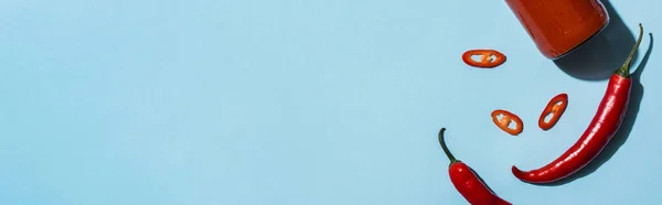 Вид зверху гострий перець чилі з кетчупом у пляшці на синій поверхні, панорамний знімок — стокове фото