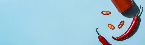 Top view of spicy chili peppers with ketchup in bottle on blue surface, panoramic shot — Stock Photo