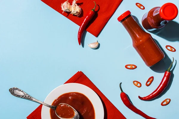 Blick von oben auf hausgemachte Chilisoße mit Knoblauch und Chilischote auf blauer Oberfläche — Stockfoto