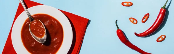 Top view of plate with spicy chili sauce and chili peppers on blue background, panoramic shot — Stock Photo