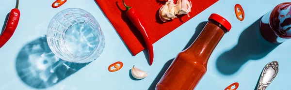 Top view of glass of water with chili peppers and ketchup on blue background, panoramic shot — Stock Photo