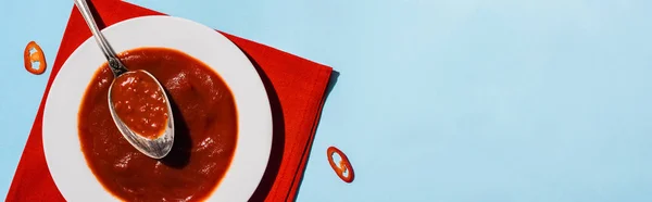 Top view of homemade chili sauce with slices of chili pepper on on blue background, panoramic shot — Stock Photo