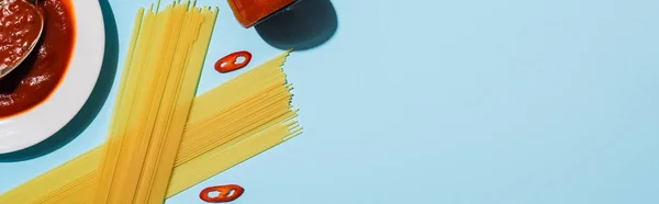 Vista dall'alto di spaghetti crudi con salsa di pomodoro su fondo blu, colpo panoramico — Foto stock