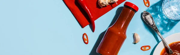 Vista dall'alto della salsa di pomodoro con peperoncino e bicchiere d'acqua sulla superficie blu, colpo panoramico — Foto stock