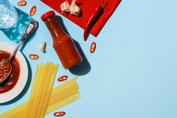 Blick von oben auf pikantes Ketchup mit Knoblauch und Chili neben Spaghetti auf blauem Hintergrund — Stockfoto