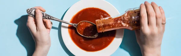 Vista recortada de la mujer vertiendo ketchup en plato con cuchara sobre fondo azul, plano panorámico - foto de stock