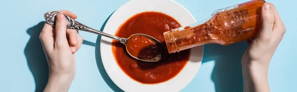 Vista ritagliata della donna versando ketchup dalla bottiglia sul piatto su sfondo blu, colpo panoramico — Foto stock