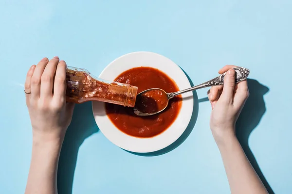 Vista cortada de mulher derramando ketchup de garrafa na placa no fundo azul — Fotografia de Stock