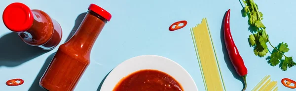Вид сверху на острый томатный соус рядом с сырыми спагетти и перцем чили на синем фоне, панорамный снимок — стоковое фото