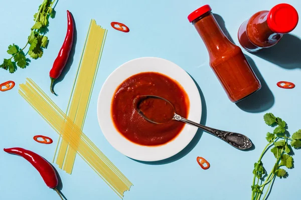 Top view of homemade chili sauce with raw spaghetti, chili peppers and cilantro on blue surface — Stock Photo