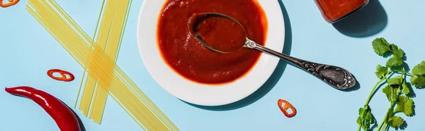 Top view of chili sauce with spaghetti, chili peppers and greenery on blue background, panoramic shot — Stock Photo