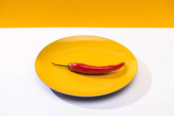 Würzige Chilischote auf Teller auf weißer Oberfläche auf gelbem Hintergrund — Stockfoto