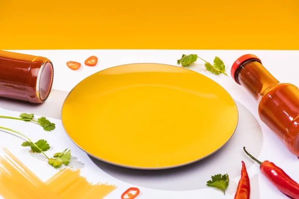 Piatto a fianco salsa di pomodoro piccante in bottiglia con spaghetti e peperoncino su fondo bianco su fondo giallo — Foto stock