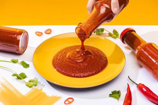 Vista cortada da mulher derramando molho de pimenta no prato com pimentão e espaguete na superfície branca isolada no amarelo — Fotografia de Stock