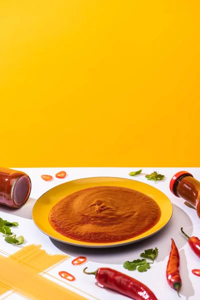 Homemade spicy tomato sauce with spaghetti and chili peppers on white surface on yellow background — Stock Photo