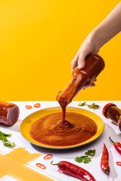 Cropped view of woman holding ketchup beside spaghetti and chili peppers on white surface isolated on yellow — Stock Photo
