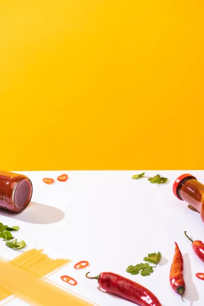 Ketchup en bouteilles avec spaghettis, piments et coriandre sur fond blanc sur fond jaune — Photo de stock