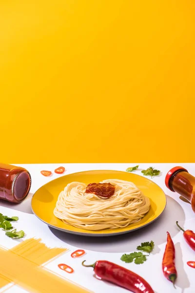 Delicious spaghetti with ketchup, cilantro and chili peppers on white surface on yellow background — Stock Photo