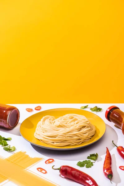 Plate with spaghetti with tomato sauce, cilantro and chili peppers on white surface on yellow background — Stock Photo