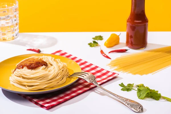 Selective focus of homemade spaghetti with ketchup, cilantro and peppers on white surface on yellow background — Stock Photo