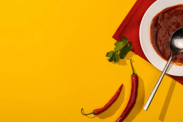 Top view of ketchup in plate with cilantro and chili peppers on yellow background — Stock Photo