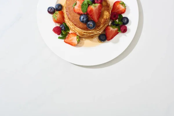 Vista superior de deliciosas panquecas com mel, mirtilos e morangos na superfície branca de mármore — Fotografia de Stock