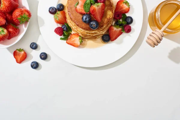 Top view of delicious pancakes with honey, blueberries and strawberries on plate on marble white surface — Stock Photo