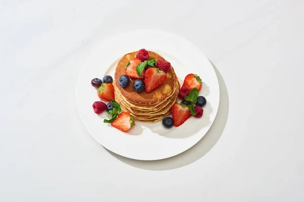 Deliciosos panqueques con miel, arándanos y fresas en plato sobre una superficie blanca de mármol - foto de stock