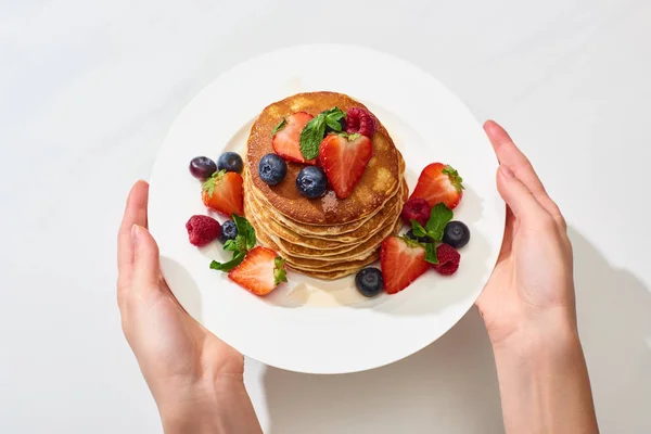 Abgeschnittene Ansicht einer Frau, die einen Teller mit leckeren Pfannkuchen mit Honig, Blaubeeren und Erdbeeren hält — Stockfoto