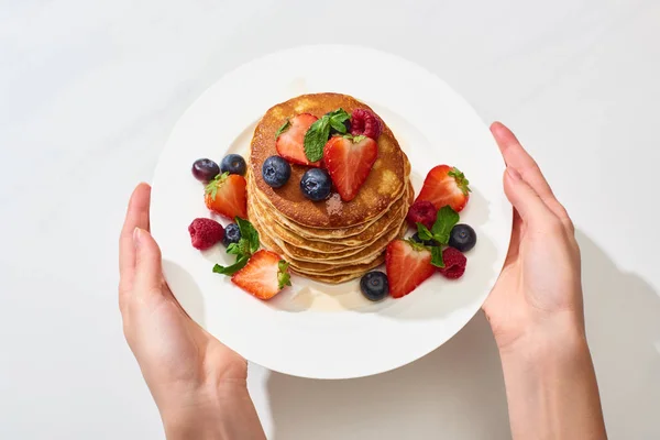 Cropped view of woman holding plate with delicious pancakes with honey, blueberries and strawberries — Stock Photo