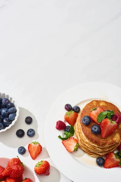 Top view of delicious pancakes with honey, blueberries and strawberries on plate on marble white surface — Stock Photo