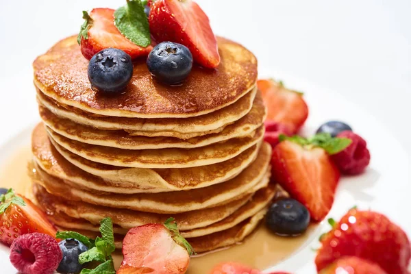 Close up view of delicious pancakes with honey, blueberries and strawberries on plate on white surface — Stock Photo