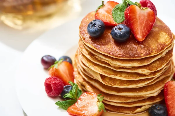 Vista de cerca de deliciosos panqueques con miel, arándanos y fresas en el plato en la superficie blanca - foto de stock