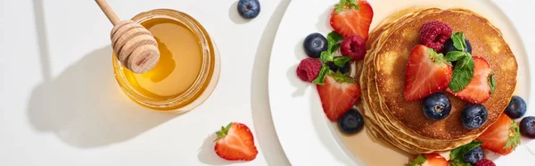 Vue de dessus des crêpes délicieuses avec du miel, des bleuets et des fraises sur plaque sur la surface de marbre blanc, vue panoramique — Photo de stock