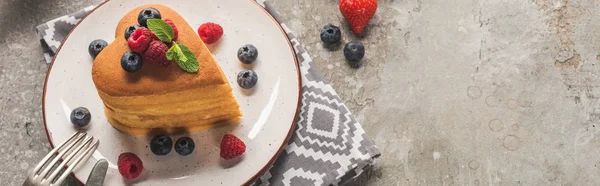 Top view of heart shaped pancakes with berries on grey concrete surface with cutlery and napkin, panoramic shot — Stock Photo