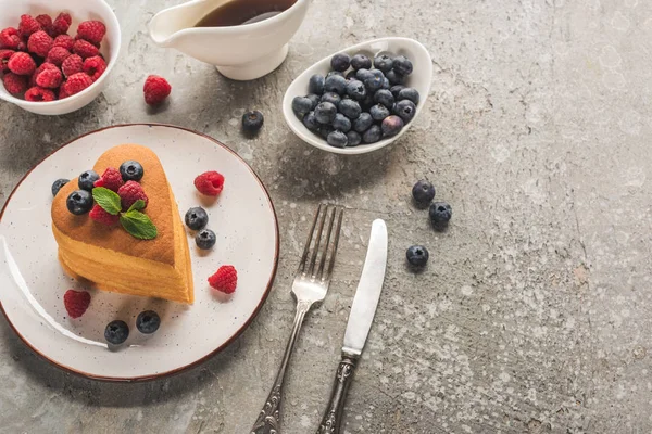 Top view of heart shaped pancakes with berries on grey concrete surface with cutlery, maple syrup — Stock Photo