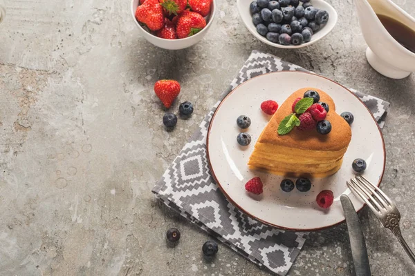 Herzförmige Pfannkuchen mit Beeren auf grauer Betonoberfläche mit Besteck, Ahornsirup und Serviette — Stockfoto