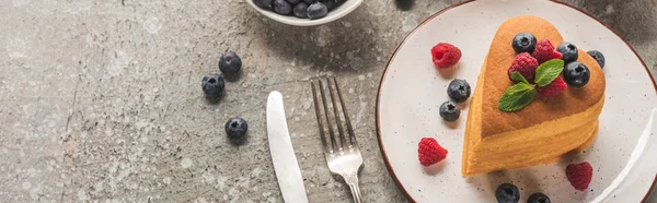 Вид зверху на млинці у формі серця з ягодами на сірій бетонній поверхні з столовими приборами, панорамний знімок — стокове фото