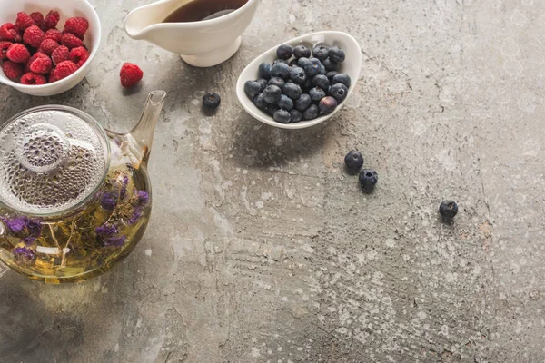 Вид сверху на ягоды, травяной чай и кленовый сироп на серой бетонной поверхности — стоковое фото