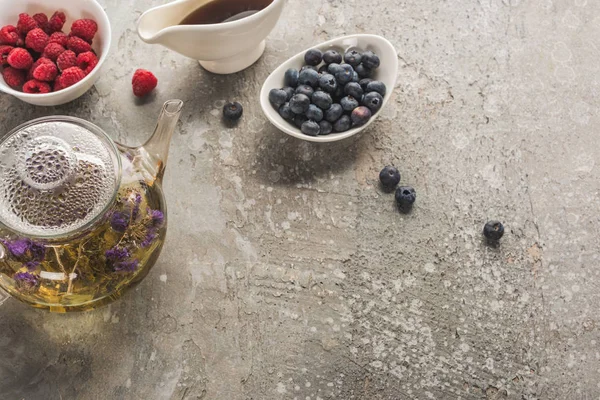 Von oben mit Beeren, Kräutertee und Ahornsirup auf grauer Betonoberfläche — Stockfoto