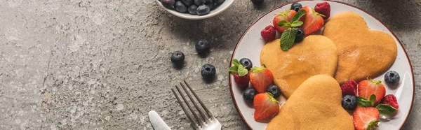 Top view of heart shaped pancakes with berries on grey concrete surface with cutlery, panoramic shot — Stock Photo