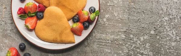 Draufsicht auf herzförmige Pfannkuchen mit Beeren auf grauer Betonoberfläche, Panoramaaufnahme — Stockfoto