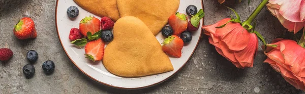 Top view of heart shaped pancakes with berries on grey concrete surface near roses, panoramic shot — Stock Photo