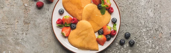 Draufsicht auf herzförmige Pfannkuchen mit Beeren auf grauer Betonoberfläche, Panoramaaufnahme — Stockfoto