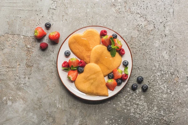 Vue de dessus des crêpes en forme de coeur avec des baies sur la surface en béton gris — Photo de stock