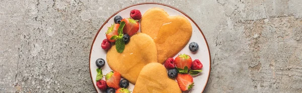 Vista dall'alto di frittelle a forma di cuore con bacche su una superficie di cemento grigio, colpo panoramico — Foto stock