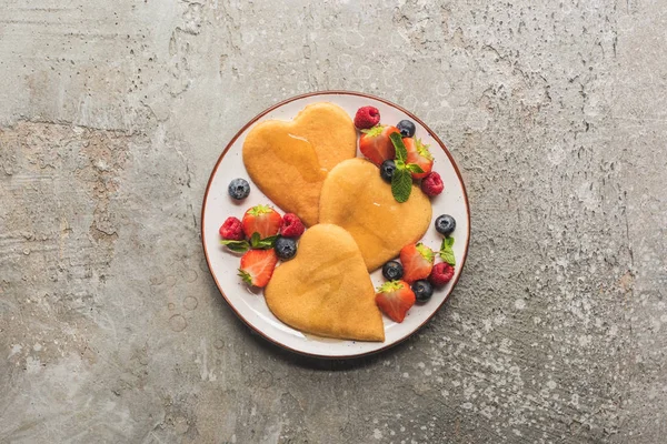 Vue de dessus des crêpes en forme de coeur avec des baies sur la surface en béton gris — Photo de stock