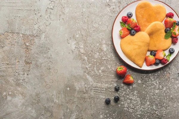 Top view of heart shaped pancakes with berries on grey concrete surface — Stock Photo